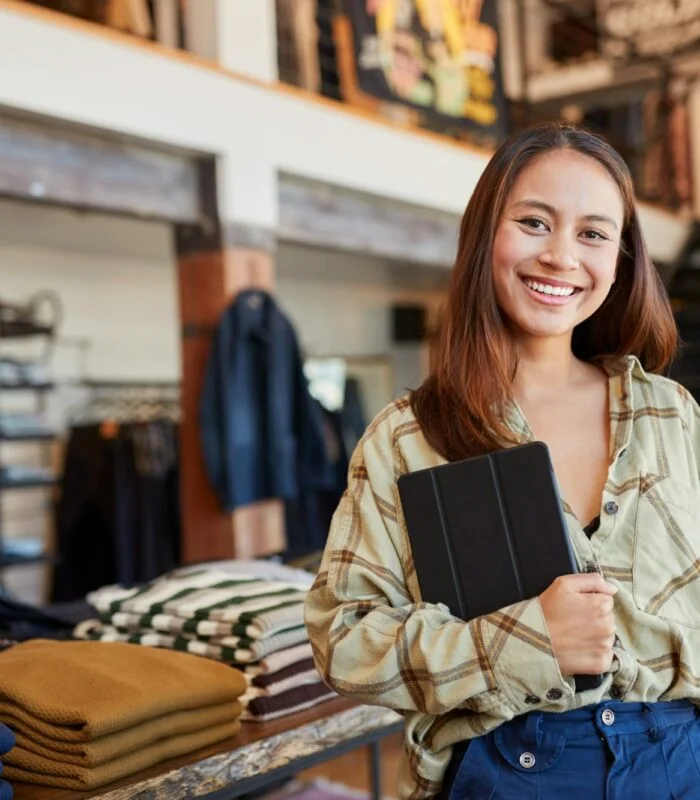 Portrait Of Female Owner Of Fashion Store Using Digital Tablet To Check Stock In Clothing Store
